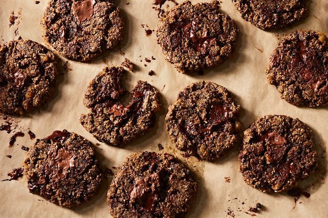 Fresh, gooey, crumbly dark brown chocolate chip cookies sit on a baking sheet.